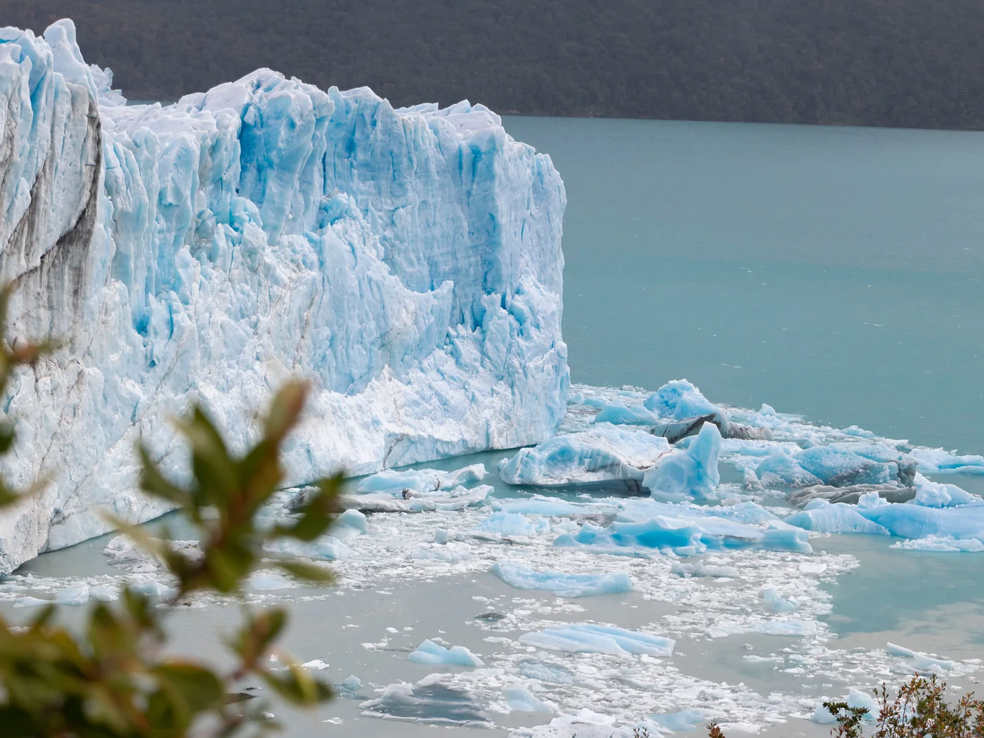 A tall blue-white glacier ice wall with floating ice at its base